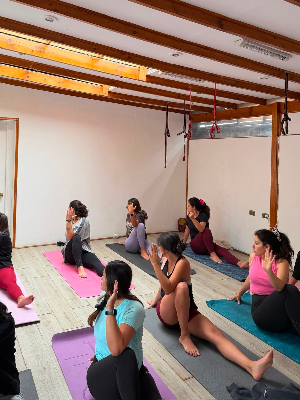 Grupo de alumnas practicando yoga juntas en sala con vigas de madera